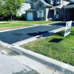 A home with new blacktop on the driveway. There is a white sign on the lawn that reads "TNT Asphalt".